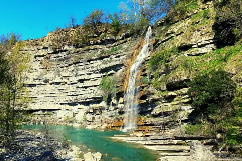 Cascate di Moraduccio: una cascata scende da una parete rocciosa stratificata, formando un arcobaleno nell'acqua turchese sottostante.