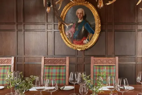 Un ritratto regale domina la sala da pranzo, con sedie a quadri e un tavolo apparecchiato, un'ambientazione che evoca i migliori ristoranti di Londra.