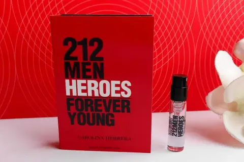 Czerwone opakowanie Carolina Herrera 212 Heroes Forever Young obok atomizera i białych kwiatów.