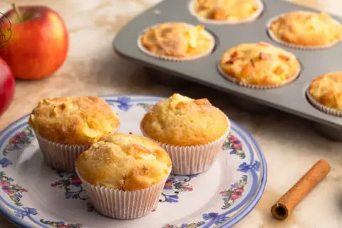 Frisch gebackene Apfelmuffins auf einem Teller, daneben Äpfel und Zimt. Ein tolles Muffins Rezept für gemütliche Stunden.