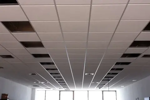Un plenum falso techo modular con paneles blancos y rejillas metálicas visibles en algunos huecos.
