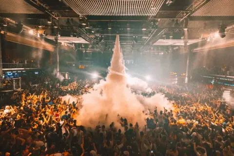 Folla in delirio in una **fabrik discoteca** con un getto di fumo che sale verso il soffitto.
