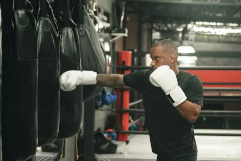 Man in white boxing gloves throws a punch at a heavy bag, demonstrating how to practice boxing without a bag.