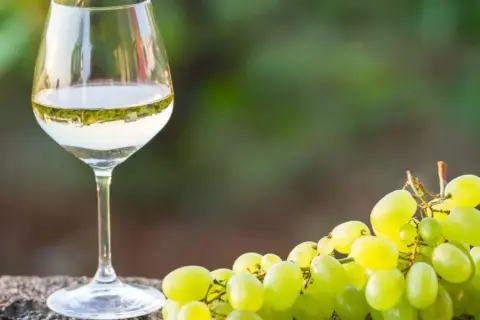 Szklanka białego wina, prawdopodobnie alvarinho, obok kiści zielonych winogron na kamiennym blacie.