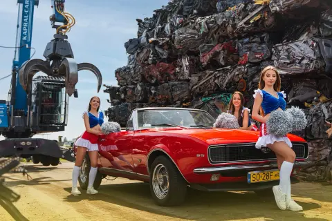 Trzy cheerleaderki z pomponami pozują przy czerwonym kabrioletcie na tle sterty złomu. To może być ciekawy widok dla kogoś szukającego auto szrot bydgoszcz.