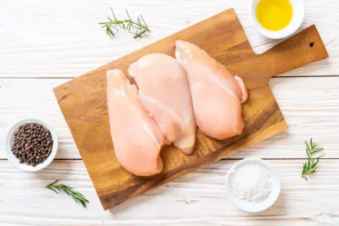 Tre petti di pollo crudi su tagliere, con pepe nero, sale, rosmarino e olio. Ideale per un pasto leggero, con poche calorie petto di pollo.