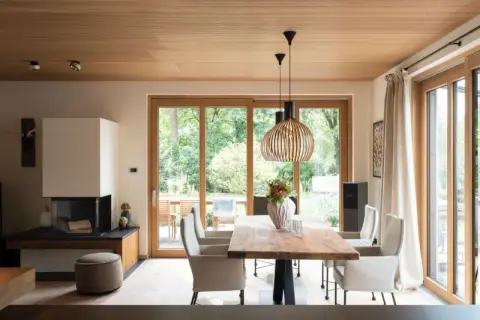 Moderne Inneneinrichtung mit viel Holz: Essbereich mit Holztisch, Kamin und großen Glasfronten zur Gartenseite.