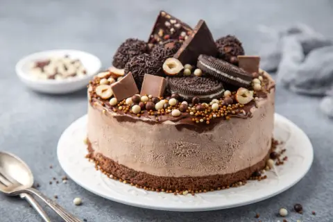 En chokladglassbakelse dekorerad med chokladbitar, oreos, hasselnötter och strössel. Enkel chokladsås rinner ner längs sidorna.