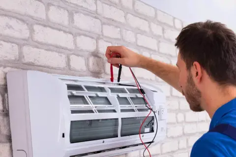 Sprawdź, jaka jest odgrzybianie klimatyzacji cena. Technik z miernikiem przy białej jednostce klimatyzacyjnej.