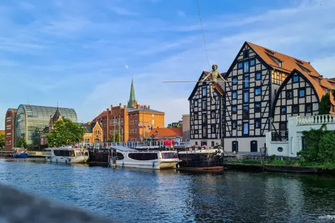 Bydgoszcz atrakcje: łodzie cumujące przy Brdzie, nowoczesna architektura i zabytkowe kamienice z postacią na linie.