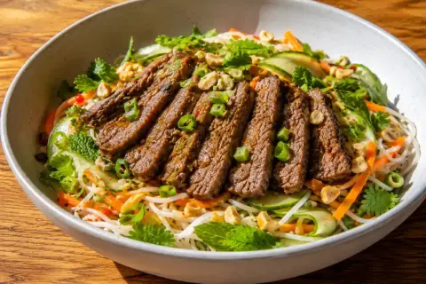 En skål med asiatisk biffsallad med nudlar, strimlad biff, gurka, morötter, mynta och jordnötter.