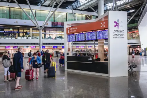 Lotnisko Chopina Warszawa. Ludzie z bagażami czekają na informacje o lotach. Ile wcześniej trzeba być na lotnisku Chopina?