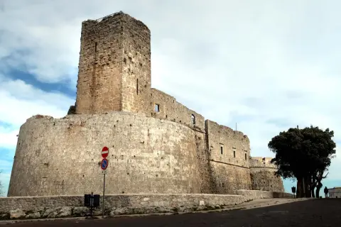 Imponente castello di Monte Sant'Angelo, con mura in pietra grezza e un torrione svettante sotto un cielo nuvoloso.
