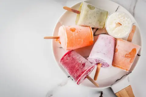 Variopinti ghiaccioli fatti in casa su un piatto bianco: rossi, arancioni, rosa, verdi e bianchi al cocco.