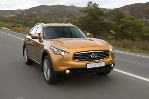 Pomarańczowy Infiniti QX70 jedzie po drodze wśród jesiennych wzgórz.