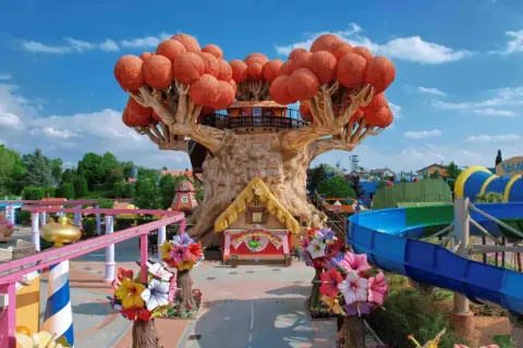 Un magico parco divertimenti in Italia con un albero gigante, scivoli acquatici e giostre colorate.