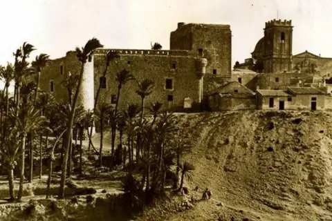 Las torres de Altamira se alzan majestuosas sobre una colina, rodeadas de palmeras. Un antiguo castillo y una iglesia vigilan el paisaje.