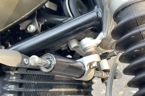 Amortyzator skrętu motocykl, zamontowany obok chłodnicy, zapewnia stabilność kierownicy podczas jazdy.