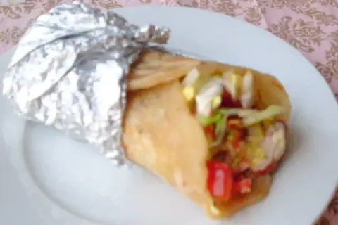 Pyszny kebab w cieście, zawinięty w folię aluminiową, z widocznymi warzywami i mięsem.
