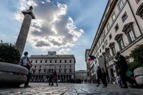 La Colonna di Marco Aurelio domina la piazza, con edifici storici e persone che passeggiano a Piazza Colonna, Roma.