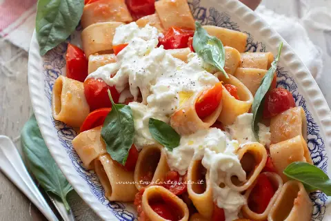 Piatto di pasta paccheri con pomodorini freschi e burrata cremosa, guarnito con basilico.
