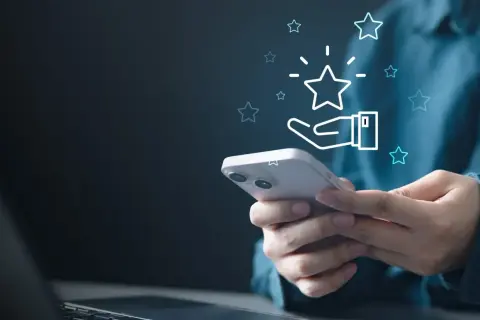 Dłoń trzymająca smartfon z ikoną gwiazdki i dłoni, symbolizującą ocenę.