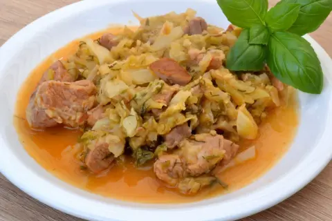 Pyszny bigos z młodej kapusty z mięsem i kiełbasą, podany na białym talerzu, ozdobiony gałązką bazylii. Idealny przepis, jak ugotować dobry bigos z młodej kapusty.