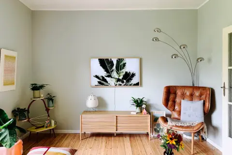 Gemütliche Wohnung mit hellen Farben: Ledersessel, Pflanzen und ein Bild mit Blattmotiv schaffen eine warme Atmosphäre.