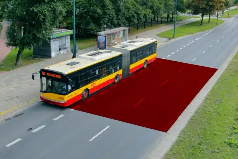 Czerwony obszar na drodze pokazuje bezpieczną odległość między samochodami w terenie zabudowanym, ilustrując przestrzeń dla autobusu.