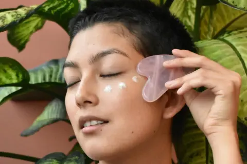 Frau mit Gua Sha Stein und Creme am Auge, genießt die feuchtigkeitsspendende Tremella Wirkung für strahlende Haut.