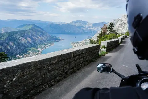 Widok z motocykla na Zatokę Kotorską w Czarnogórze. Kręta droga, kamienny mur i zapierająca dech w piersiach panorama gór i morza.