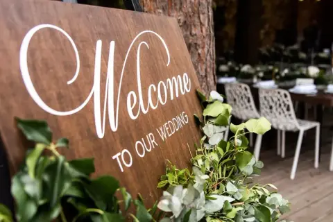 Drewniana tablica "Welcome to our wedding" z zielonymi liśćmi. Zastanawiasz się, kogo zaprosić na wesele?