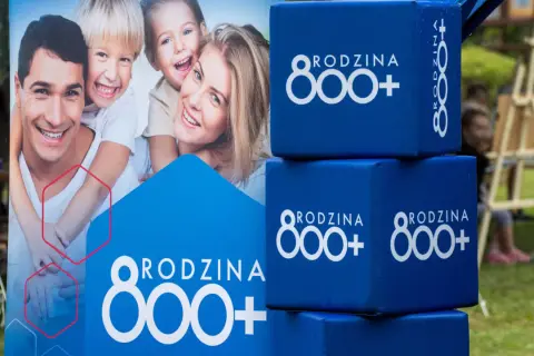 Uśmiechnięta rodzina na plakacie i niebieskie kostki z napisem "RODZINA 800+". Wniosek ZUS o świadczenie 800 plus to wsparcie dla rodzin.