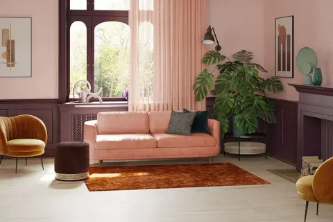 Przytulny salon z sofą w kolorze pudrowy róż, aksamitnym fotelem i dywanem w odcieniu cegły.