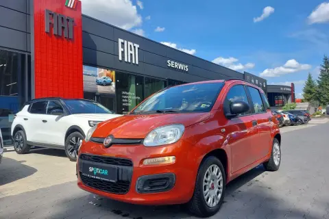 Pomarańczowy fiat panda używany z salonu czeka na nowego właściciela. Obok biały SUV.