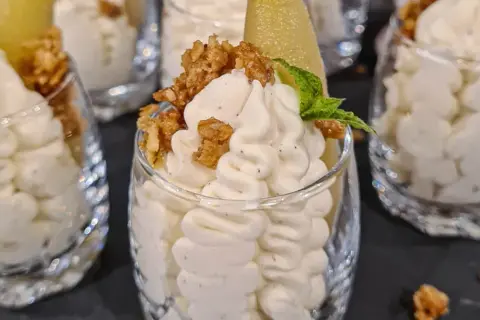 Ljuvlig vispad pannacotta i glas, toppad med krispiga nötter och en bit päron. En perfekt dessert!