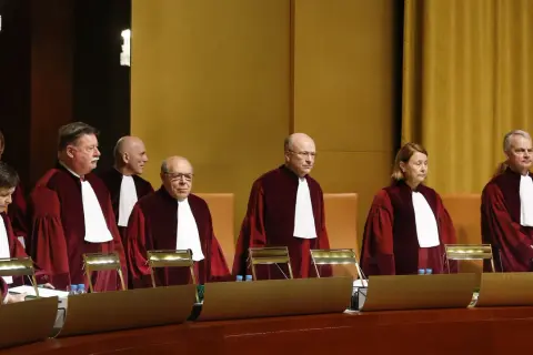 Siedmiu sędziów w togach, w tym jedna kobieta, stoi w sali sądowej. Wszyscy mają na sobie białe żaboty. W tle widać złote zasłony.