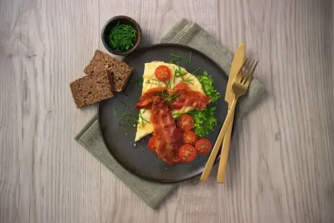En härlig omelett i ugn med knaperstekt bacon, färska tomater, sallad och grovt bröd. Serveras med gräslök.