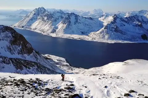 Ein Skifahrer genießt die atemberaubende Aussicht auf die schneebedeckten Berge und das tiefblaue Meer im **Lofoten Winter**.