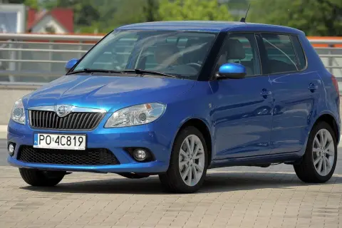 Niebieska Skoda Fabia 2, z nowymi żarówkami w reflektorach, parkuje na placu.