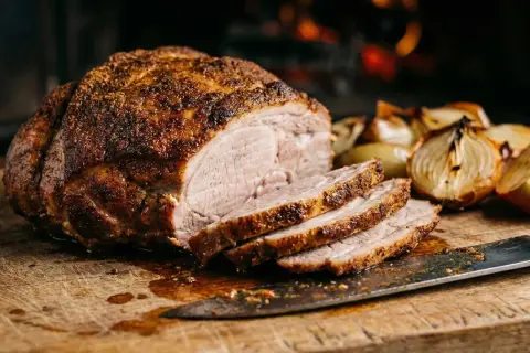 Saftiges, **schnelles Fleisch aus dem Ofen**, perfekt geschnitten, mit gerösteten Zwiebeln und einem Messer auf einem Holzbrett.