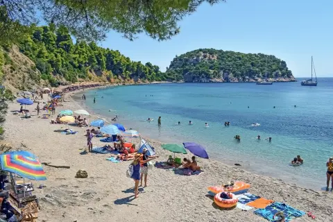 Słoneczny dzień na plaży w Chalkidiki. Ludzie opalają się, pływają w turkusowej wodzie, a kolorowe parasole rzucają cień.