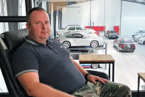 Robert Michalski, w wieku około 40-50 lat, siedzi w czarnym fotelu. W tle widać kolekcję samochodów.