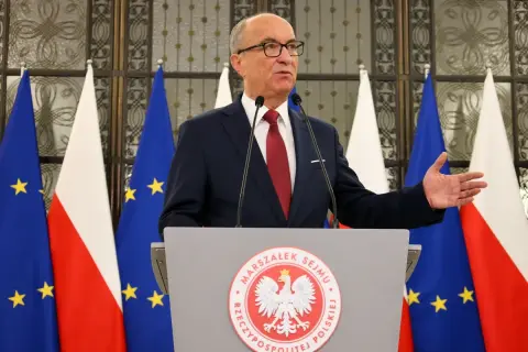 Marszałek Sejmu przemawia na tle flag Polski i UE, gestykulując. Mowa dotyczy odrzucenia weta prezydenta.