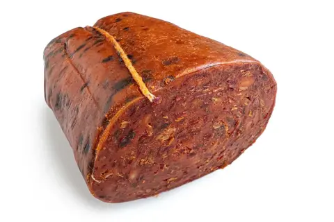 Ein Stück Nduja, eine kalabrische Streichwurst, mit grober Textur und roter Farbe, an einem Faden gebunden.