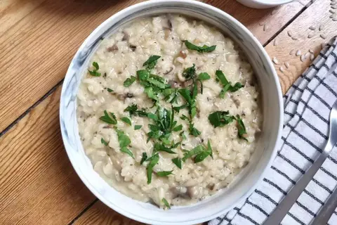 Kremowe risotto z grzybami, przygotowane w Thermomixie, posypane świeżą natką pietruszki. Idealne danie na obiad.