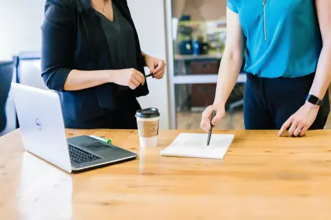 Dwie kobiety omawiają umowę ramową przy biurku z laptopem i kawą.