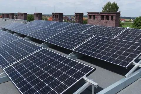 Solidna konstrukcja PV na dach płaski, z panelami ustawionymi pod optymalnym kątem do słońca. W tle kominy i zabudowania.