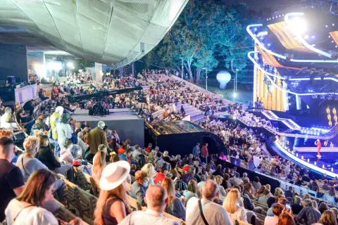 Tłumy widzów na amfiteatralnych trybunach podczas festiwalu w Opolu. Na scenie widowiskowe oświetlenie i dekoracje.