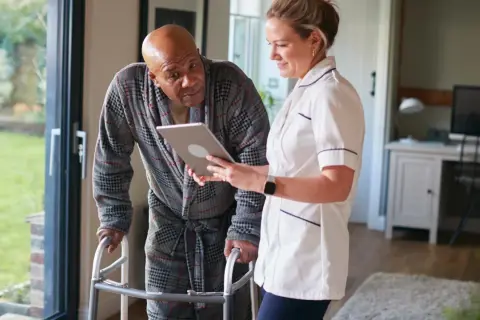 Pflegekraft zeigt Mann mit Gehhilfe auf Tablet, wie oft kann man eine Reha beantragen.